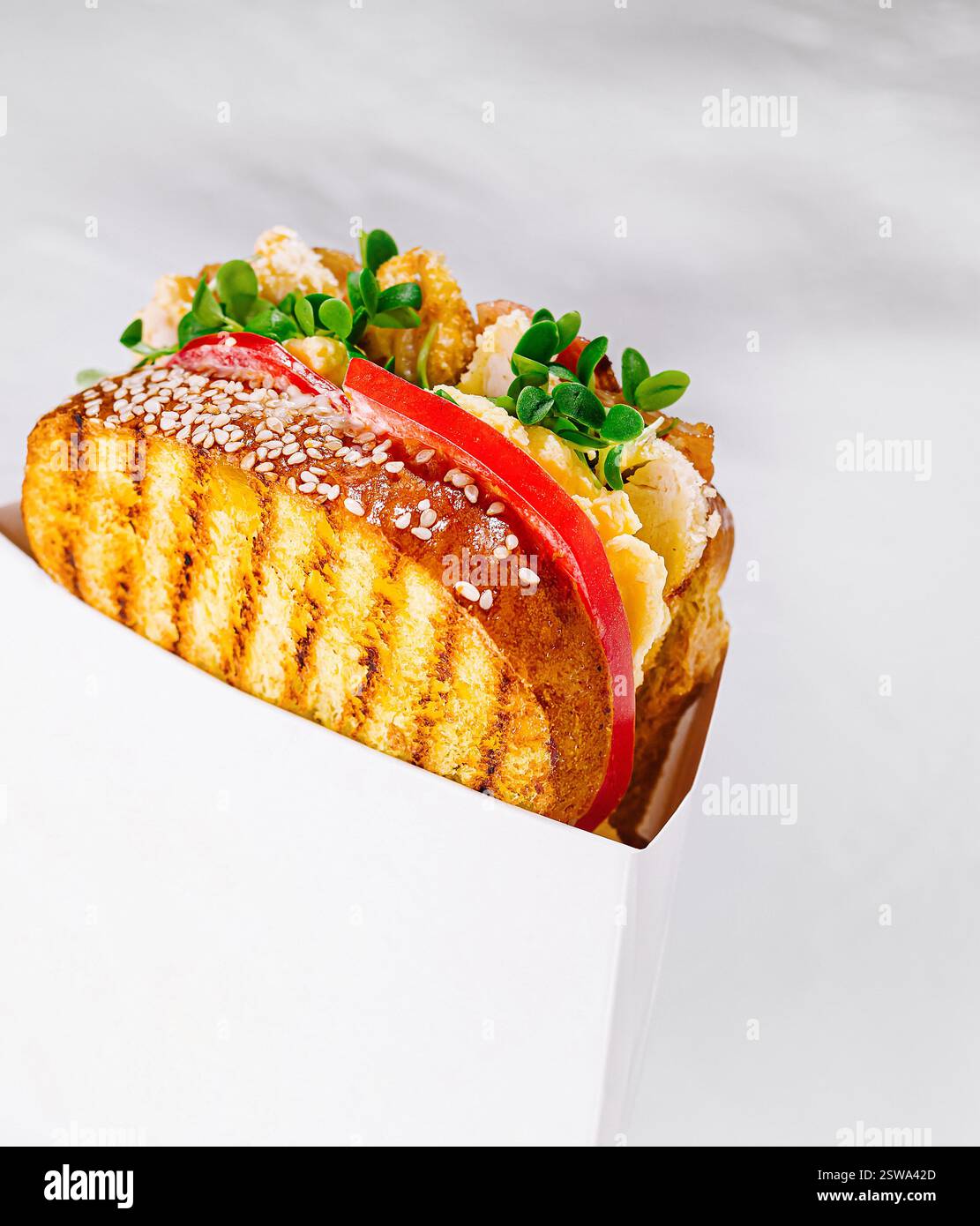 Delizioso panino tostato con pollo e verdure in scatola di cartone bianca su sfondo bianco Foto Stock