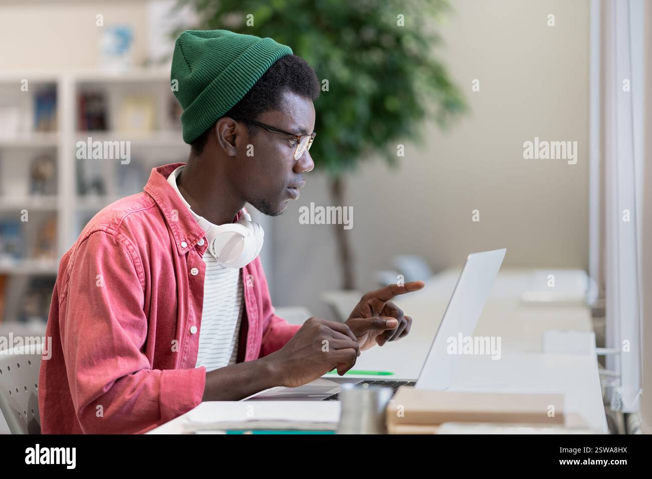 Un uomo afroamericano concentrato e autosufficiente siede a tavola con un computer portatile che sta imparando a distanza Foto Stock