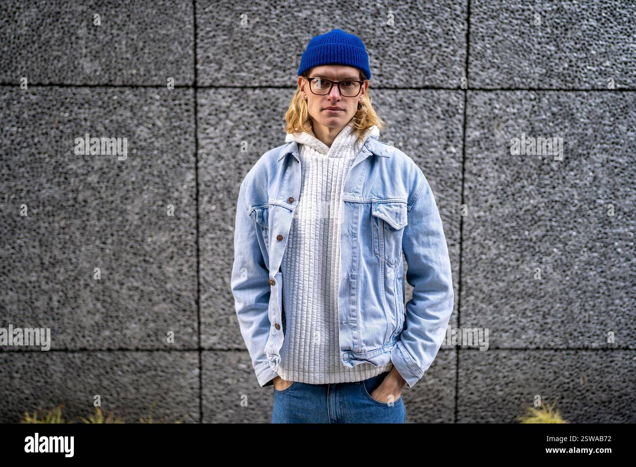 Biondo, capelli lunghi, aspetto scandinavo androgino negli occhiali in piedi sulla strada. Foto Stock