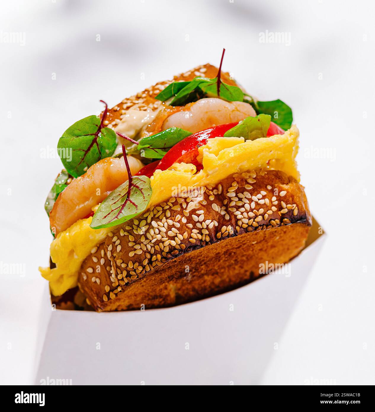 Delizioso panino tostato con gamberetti, uova strapazzate e insalata in una scatola di cartone bianca per la consegna Foto Stock