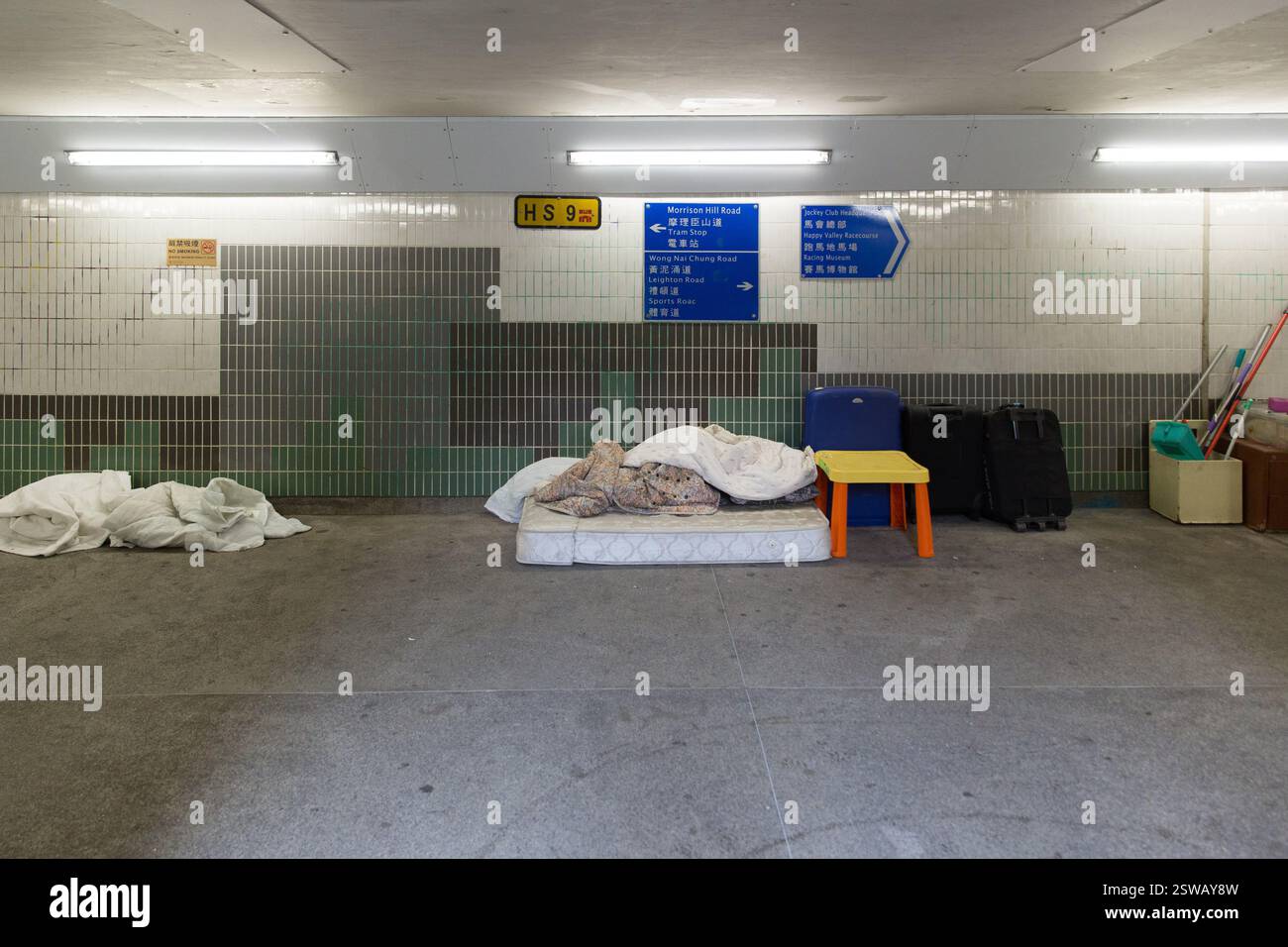 Gli effetti personali dei senzatetto, tra cui un materasso e un bagaglio, si trovano in un sottopassaggio della metropolitana alla stazione di Wong Nai Chung Road a Hong Kong. Segni indi Foto Stock
