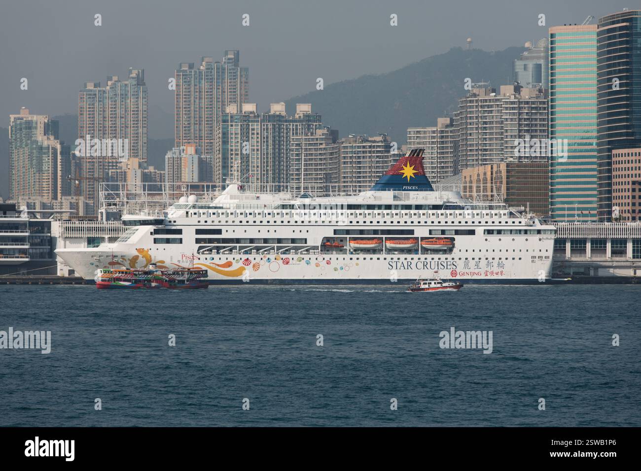 Star Cruises nave 'pesci' nel porto di Hong Kong, vicino a grattacieli e montagne. È visibile anche un traghetto più piccolo. Foto Stock