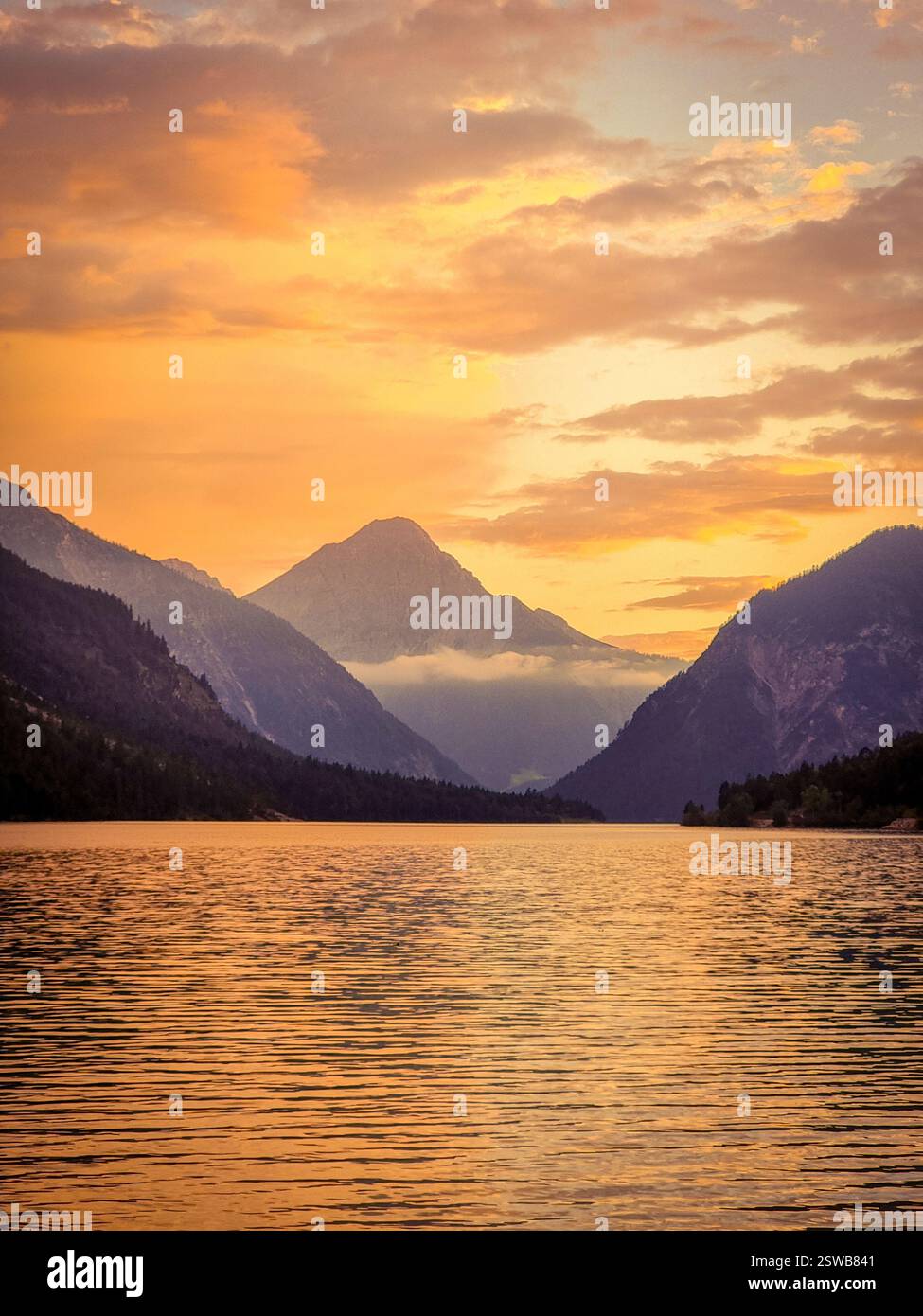Riflessi dorati al tramonto su un lago tranquillo circondato da montagne maestose Foto Stock