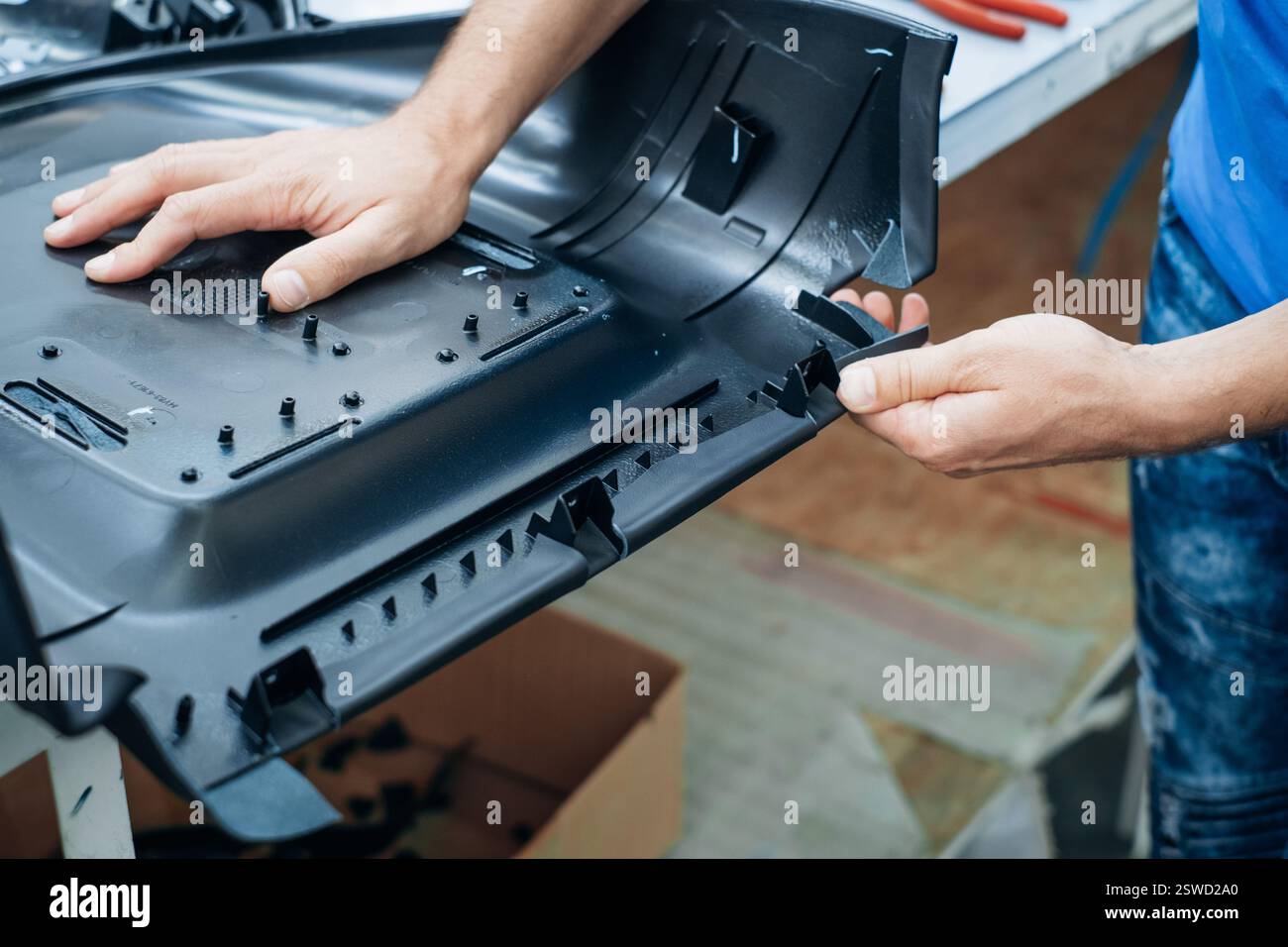Una persona lavora con le mani assemblando un intricato componente in plastica nera in un ambiente industriale Foto Stock