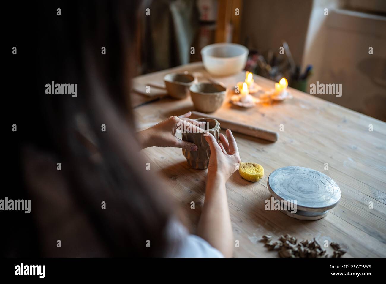La donna ceramista modella la tazza in argilla con motivo decorativo su un tavolo in legno in officina. Fai da te, master class Foto Stock