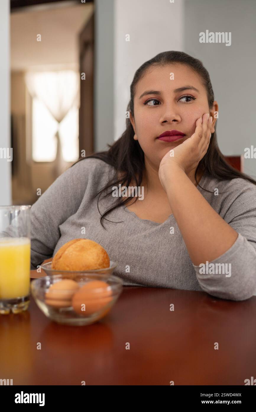 Una donna stanca si siede in un ristorante, aspettando un cucchiaio per godersi la sua colazione. La sua stanchezza è visibile mentre non vede l'ora di iniziare il suo pasto. Foto Stock