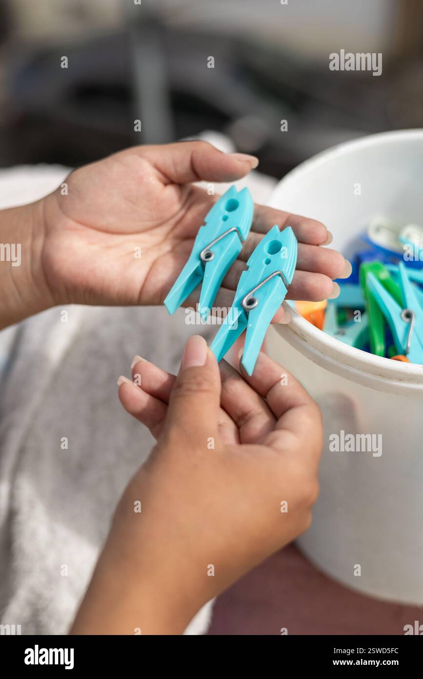Le mani di una persona raccolgono delicatamente le spille da un cestino, catturando l'atto intimo e quotidiano di fare il bucato a casa. Foto Stock