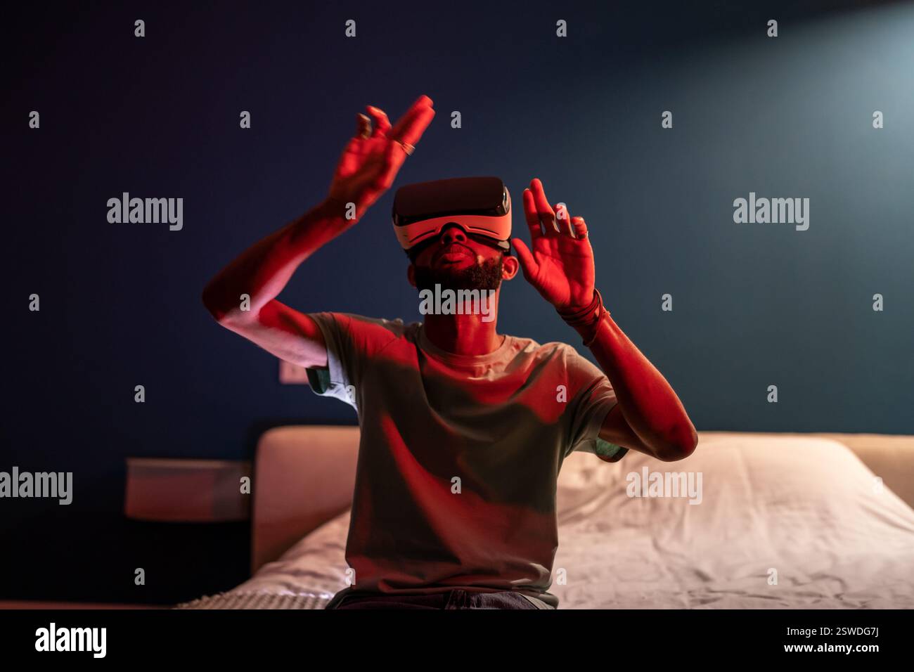 Uomo nero che indossa cuffie per realtà virtuale seduto a letto a casa per esplorare il metaverse. Concetto di realtà virtuale Foto Stock