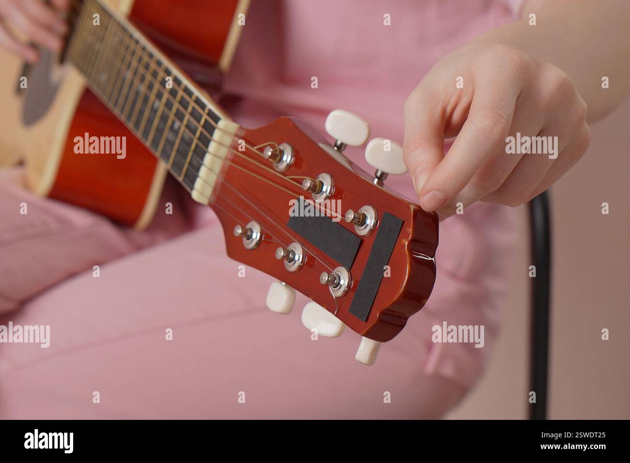 Primo piano estremo delle mani di donna che sintonizzano la chitarra acustica a sei corde, stringono e allentano la corda prima di iniziare a suonare la chitarra classica. Foto Stock