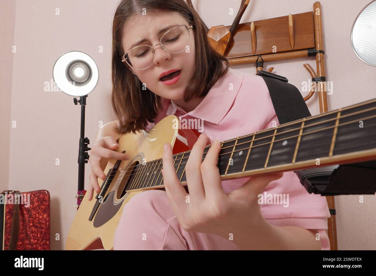 Giovane donna che suona la classica chitarra acustica a sei corde e canta, che succhia le corde emotivamente e che scuote testa a ritmo di musica pulsante. F Foto Stock