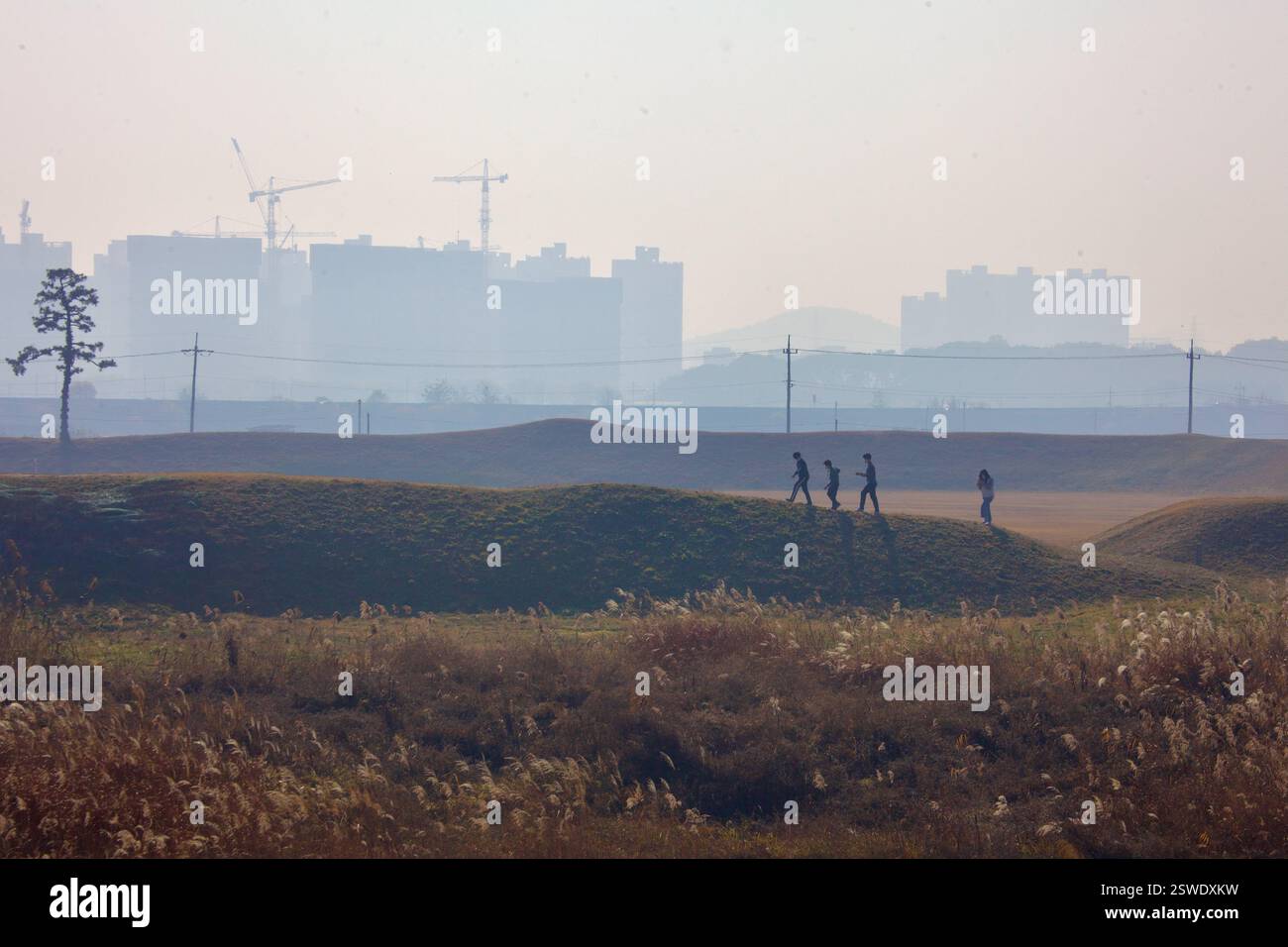Cheongju, Corea del Sud - 11 novembre 2020: Un gruppo di visitatori cammina lungo le erbose mura di terra della fortezza di Jeongbukdong Toseong, con una città nebulosa Foto Stock