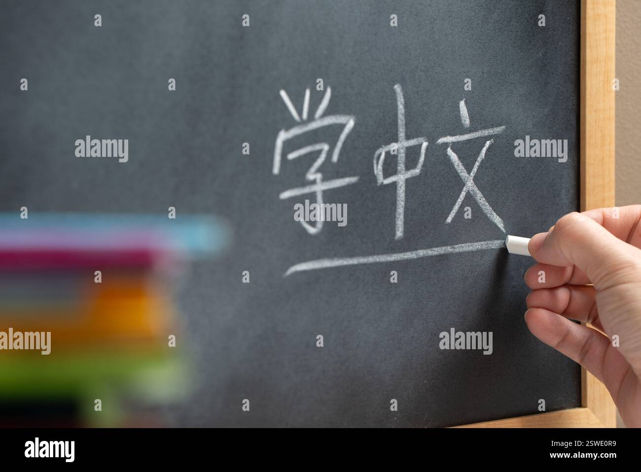 Scrittura a mano su una lavagna in una classe di lingua cinese con la parola Learn mandarin scritta sopra. Alcuni libri e materiale scolastico. Foto Stock