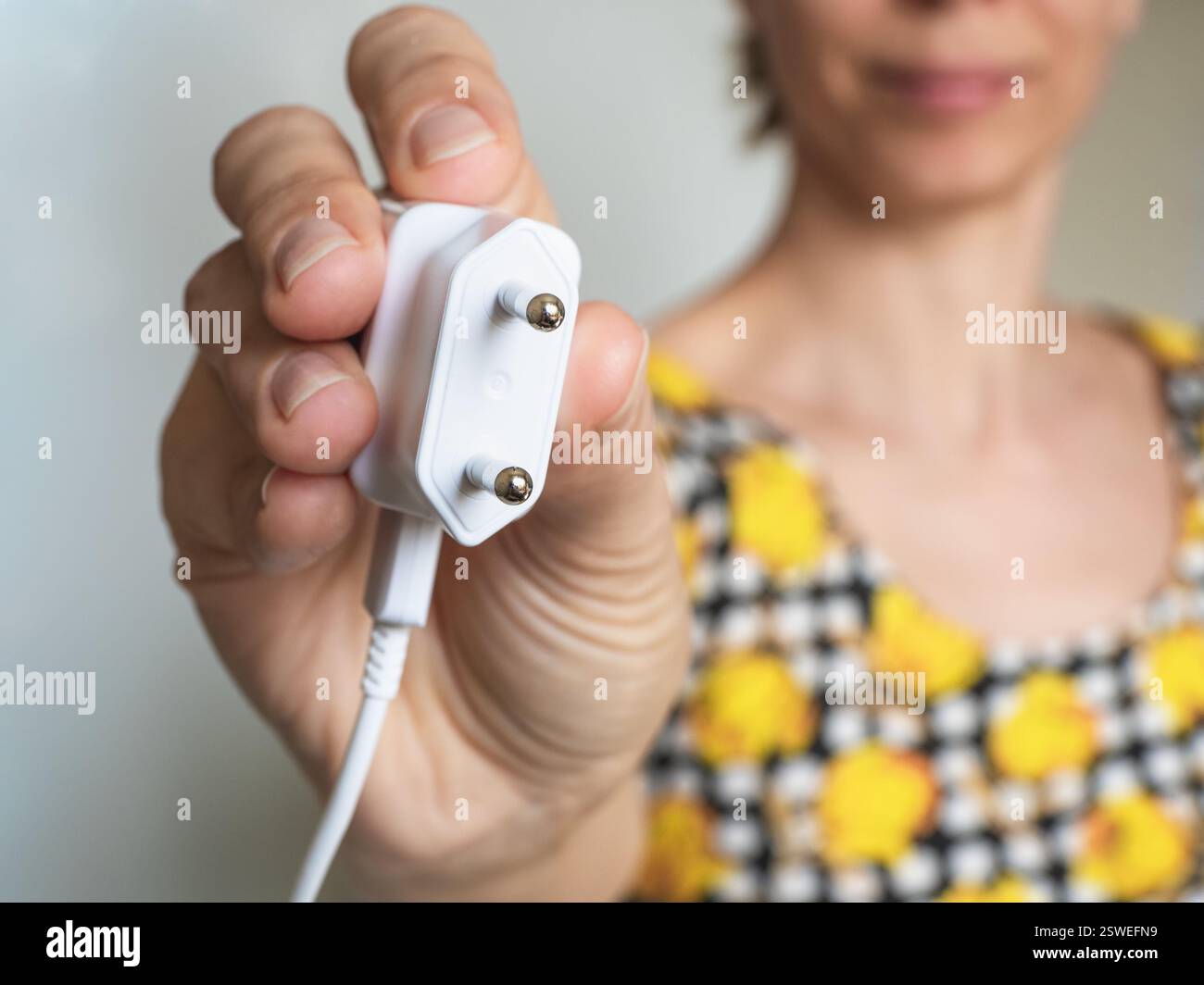 Donna che tiene la spina elettrica con la mano. Primo piano. Risparmio energetico di energia elettrica per ore sulla terra. Foto Stock