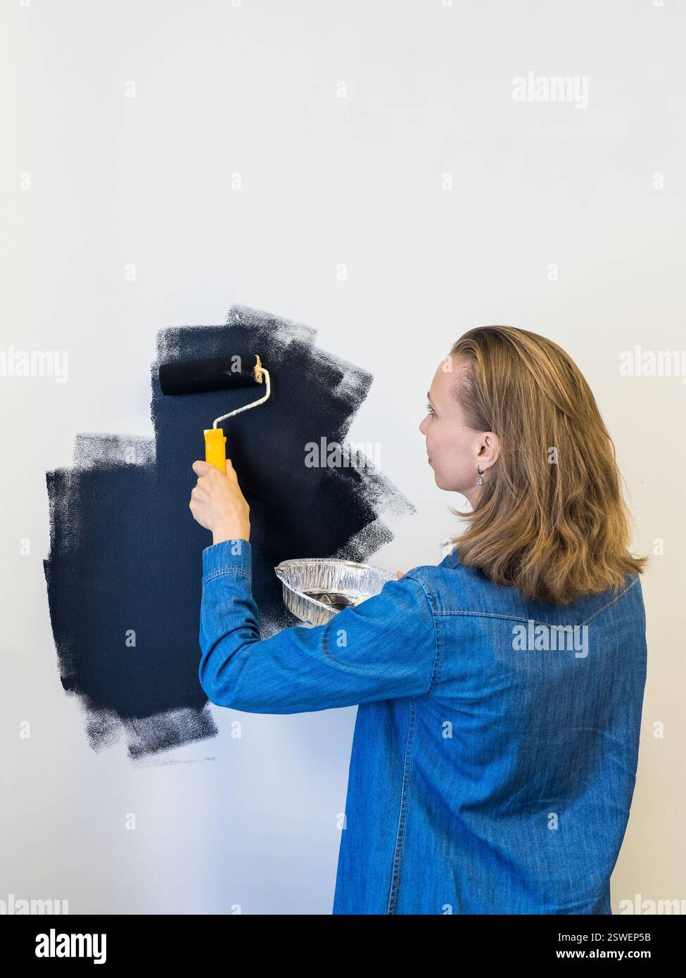 Donna che dipinge un muro in nero. Copia spazio. Vista verticale. Foto Stock