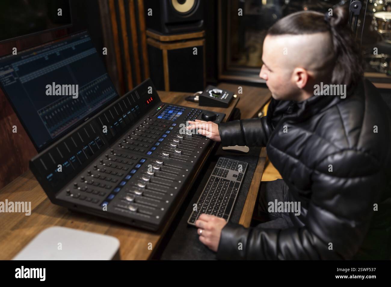 Giovane produttore musicale che mixa tracce audio utilizzando una workstation audio digitale e regola i livelli su una console di missaggio in uno studio di registrazione professionale Foto Stock