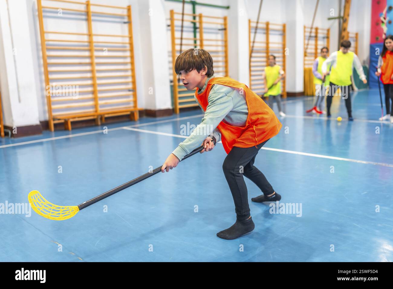 Studente della scuola elementare che gioca a floorball in classe di palestra, sviluppando la coordinazione della mano degli occhi e le abilità di lavoro di squadra Foto Stock