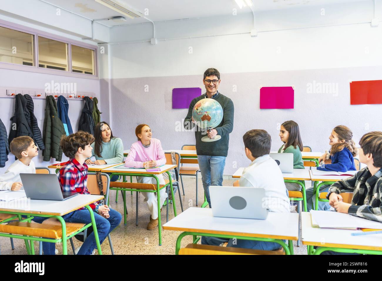 Insegnante di geografia che coinvolge gli studenti tenendo un globo, promuovendo l'apprendimento e la comprensione in un ambiente scolastico vivace Foto Stock