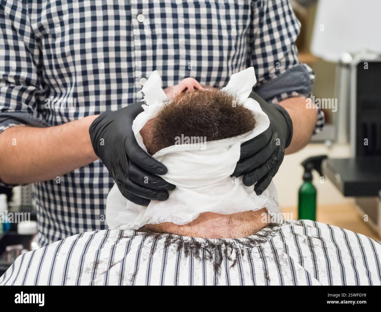 Barber mette un asciugamano caldo sul viso di mans prima di dargli la rasatura nel barbiere. Foto Stock