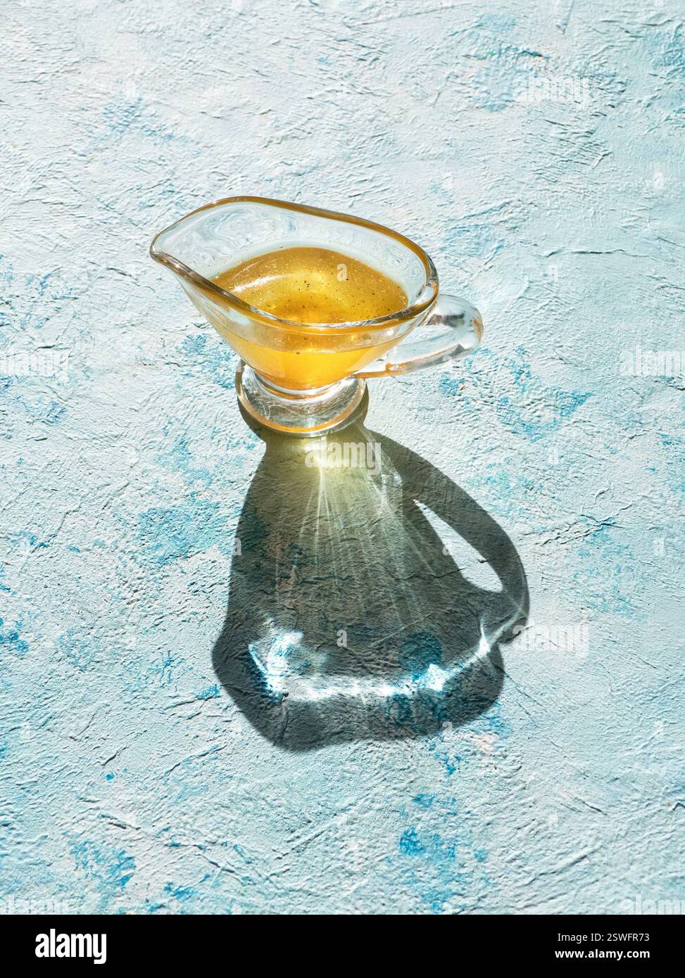 Olio in un vaso di vetro su un tavolo blu. Foto Stock