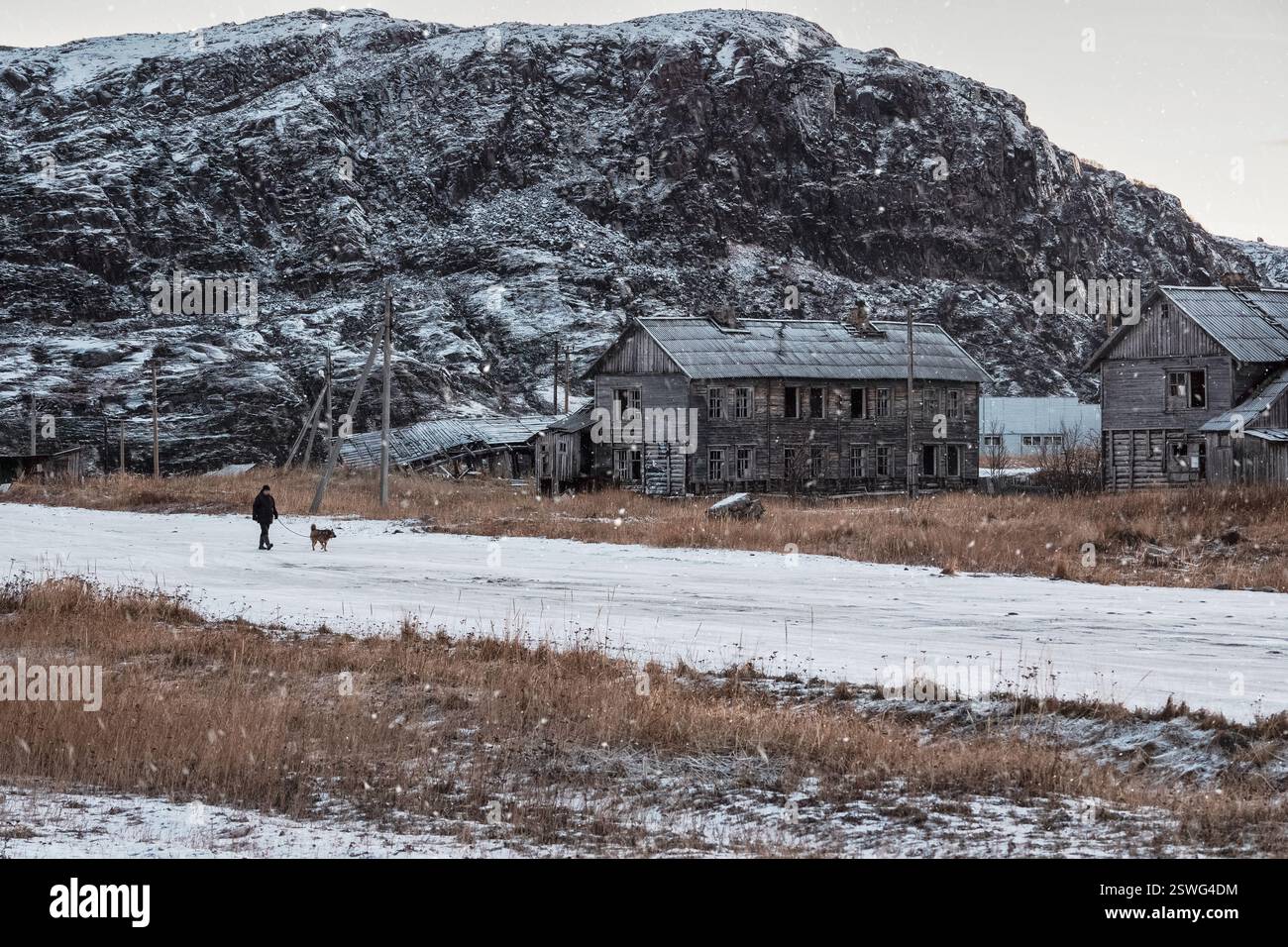 Autentico villaggio russo del nord, vecchie case in legno fatiscenti, aspra natura artica. Un uomo cammina con un cane. Teriberka. Russi Foto Stock