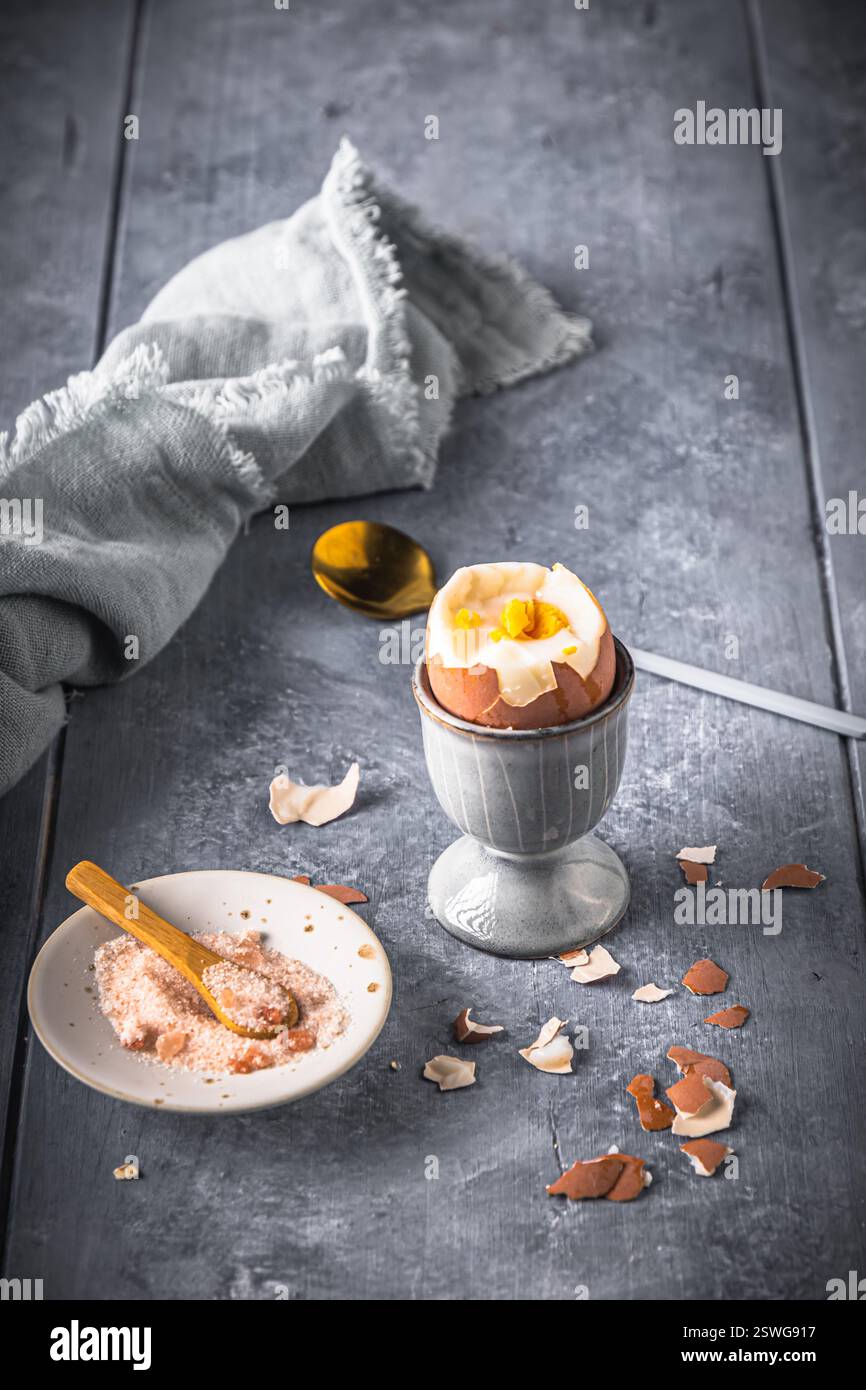 Uovo bruno sodo in cui la parte superiore è tagliata in una tazza grigia su sfondo grigio, verticale con spazio per la copia Foto Stock