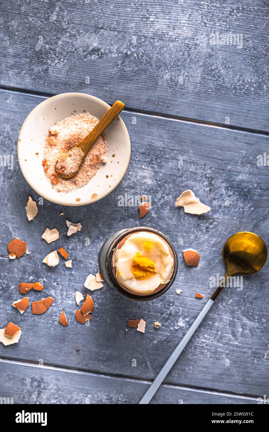Uovo bruno sodo in cui la parte superiore viene tagliata in una tazza grigia su sfondo grigio, vista dall'alto, spazio di copia Foto Stock