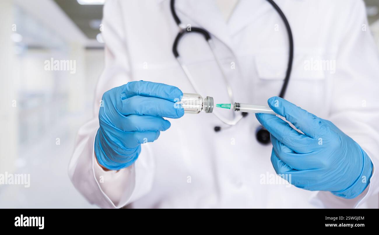 Un operatore sanitario qualificato in guanti sta aspirando il liquido vaccino in una siringa in una clinica ben illuminata. Foto Stock