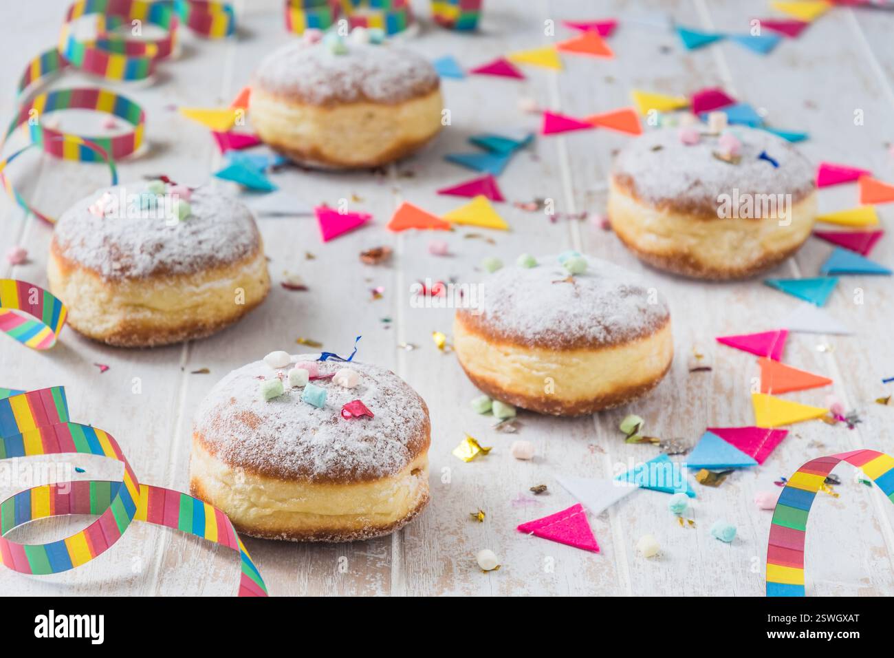 Krapfen, Berliner o ciambelle con streamers, confetti e mini marshmallows su sfondo bianco in legno. Immagine colorata di carnevale o compleanno. Foto Stock