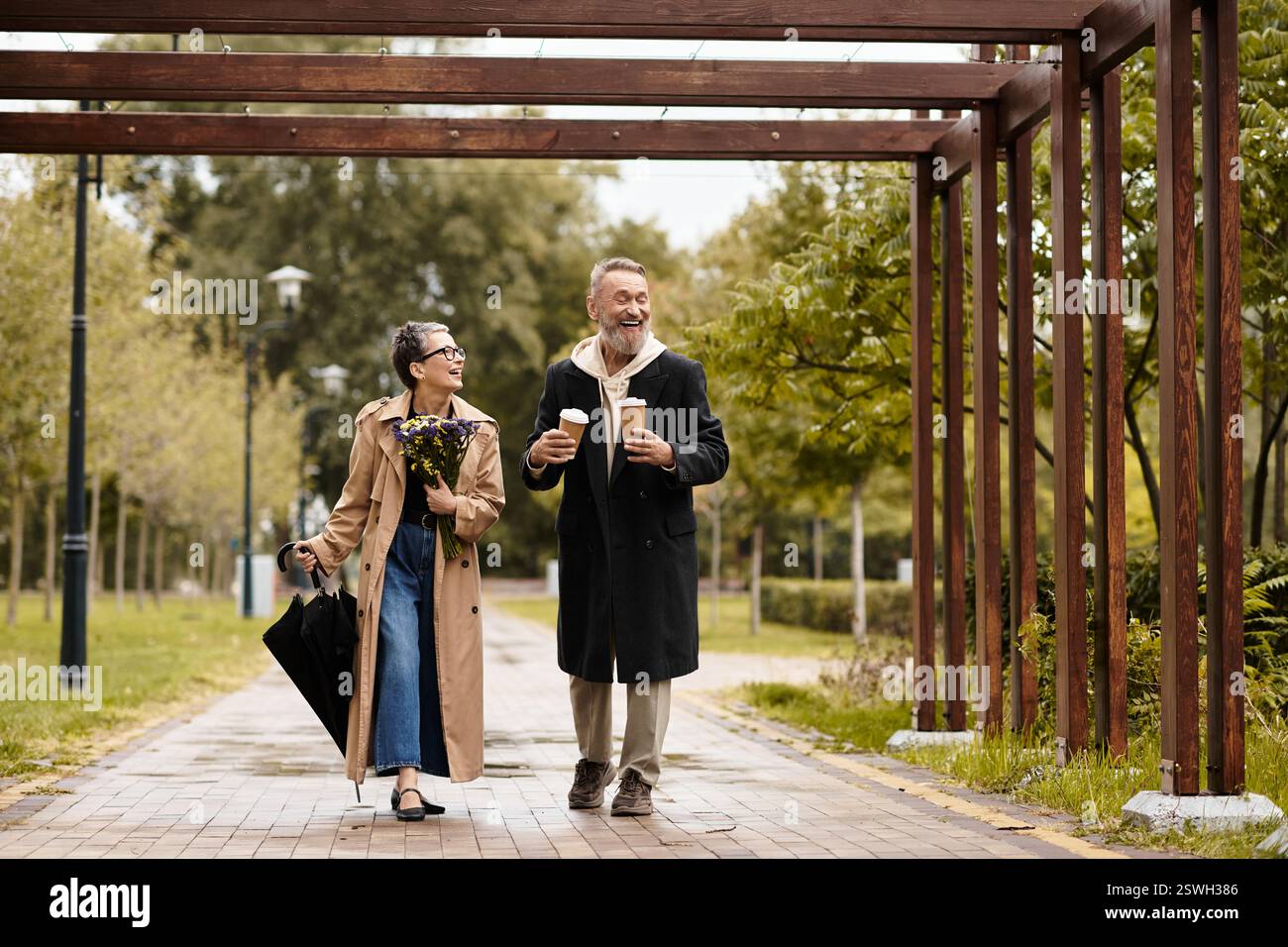 Un paio cammina di mano in mano in un parco, gustando bevande calde e sorrisi. Foto Stock