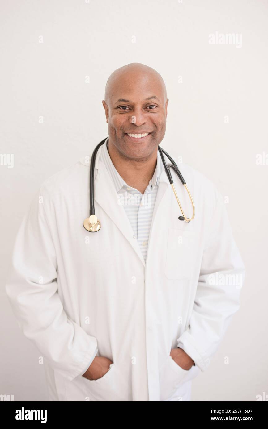 Medico sorridente in un cappotto bianco con uno stetoscopio, pronto ad aiutarti Foto Stock