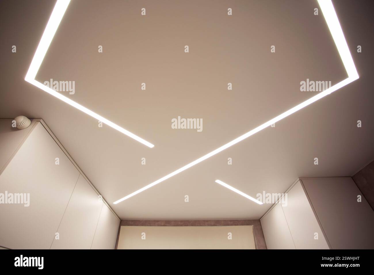 Soffitto allungato di design moderno con linee LED illuminate in camera. Foto Stock
