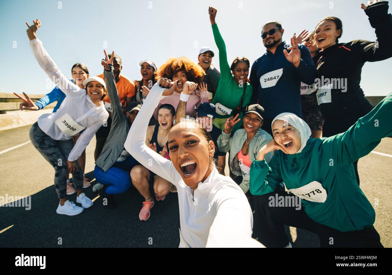 Un gruppo eterogeneo di amici si fa un selfie insieme prima di iniziare una gara. Con entusiasmo ed energia, posano in una giornata di sole, indossando la gara B. Foto Stock
