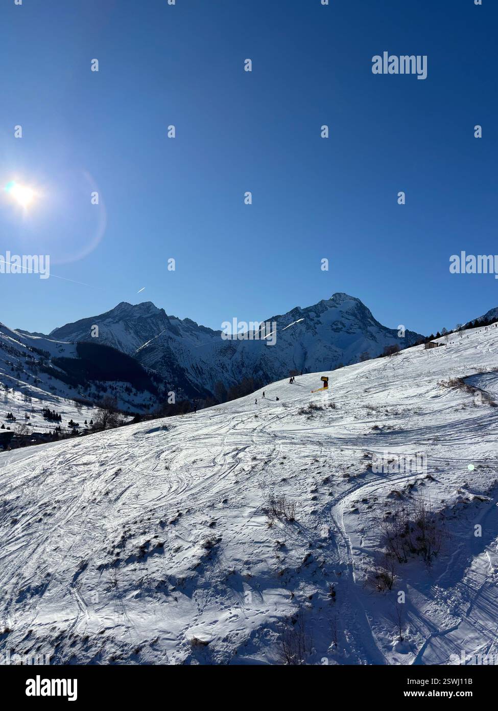 Uno splendido paesaggio di montagna innevato con piste da sci, sciatori e luce solare brillante su un cielo blu cristallino, incorniciato da aspre vette sullo sfondo - Immagine stock catturata con smartphone