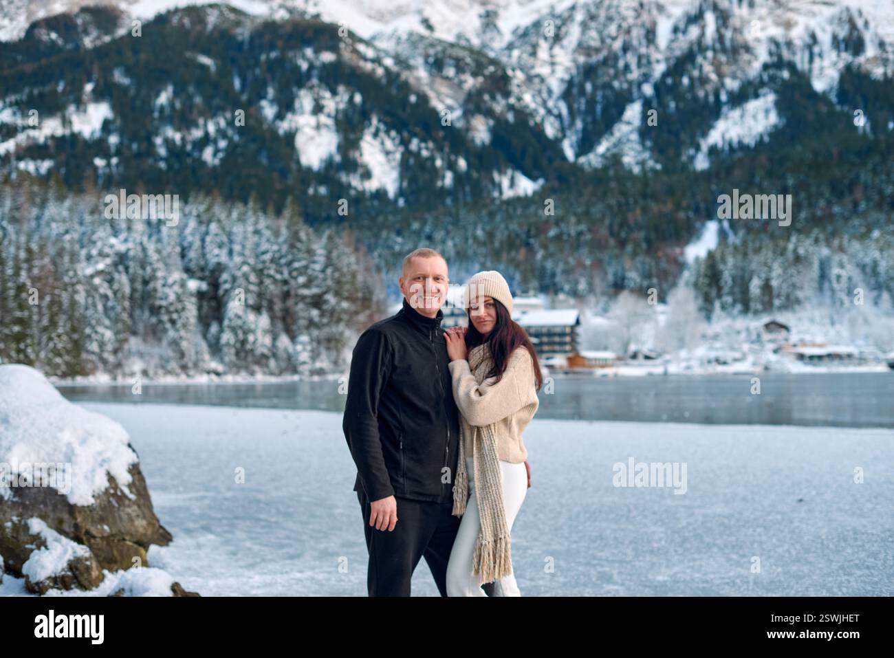Romantica vacanza invernale sul lago alpino ghiacciato con le montagne innevate e la Rustic Cabin. Serene Outdoor Ritratto di uomo in Black Fleece e donna i Foto Stock