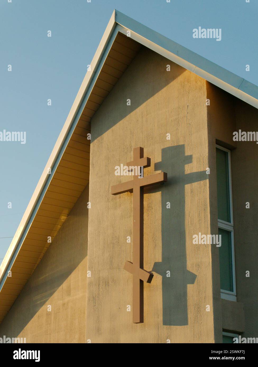 Croce cristiana ortodossa con tre travi trasversali orizzontali. Il più basso inclinato verso il basso. Quasi al tramonto con una grande ombra di croce. Verticale angolato Foto Stock
