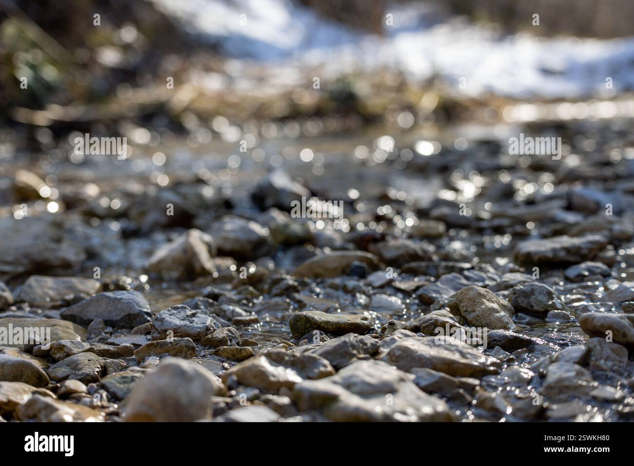 Flusso poco profondo che scorre sulle rocce con neve sullo sfondo Foto Stock