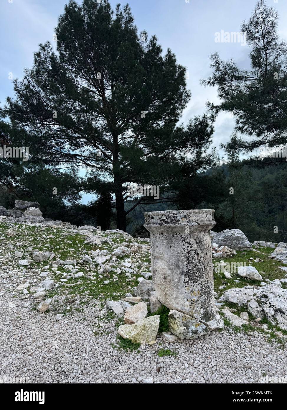 Colonne di pietra intemprate rimangono in un'area rocciosa, circondata da alberi e rovine storiche in un ambiente sereno Foto Stock