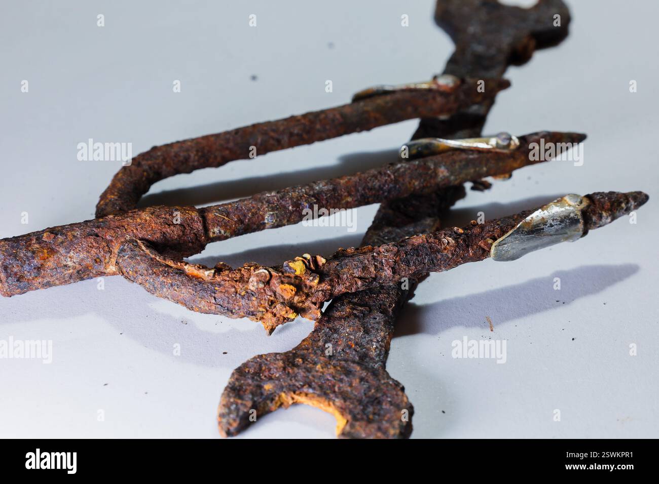 Primo piano di un tridente arrugginito che poggia su una chiave corrosa su uno sfondo bianco. Foto Stock