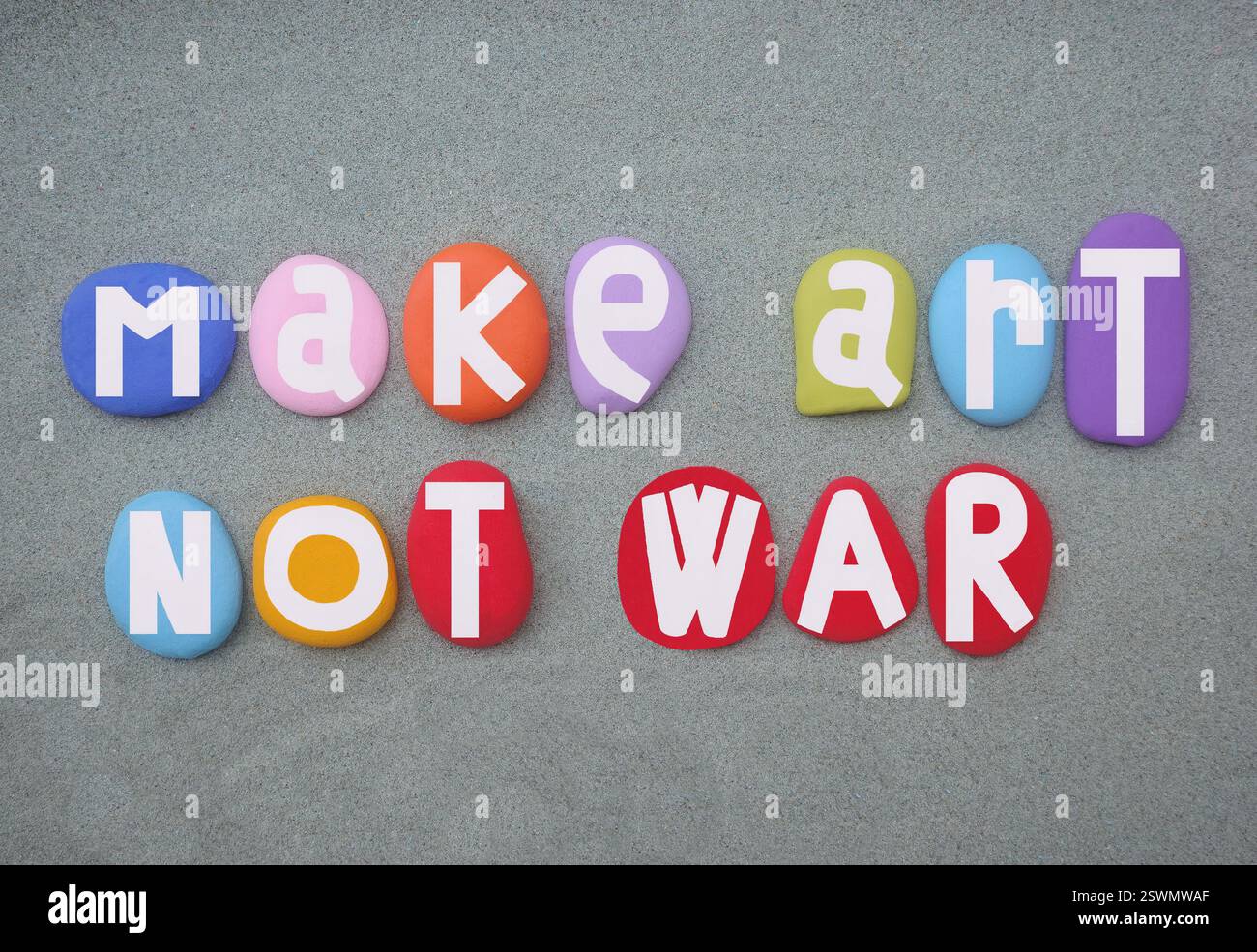 Fai arte non guerra, slogan di pace creativa composto da lettere in pietra dipinte a mano multicolore su sabbia verde Foto Stock