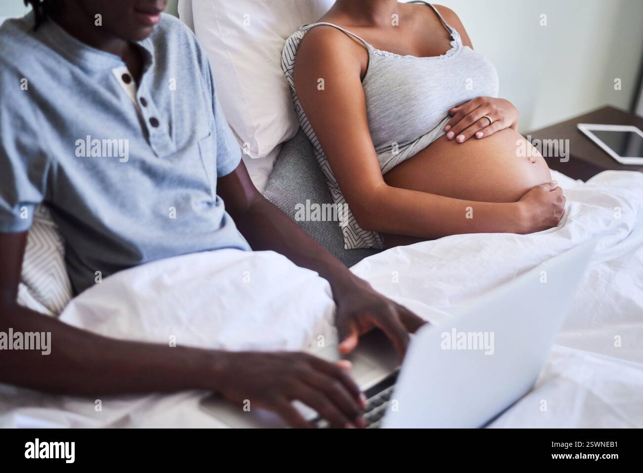 Mani, laptop e gravidanza con coppia a letto insieme per la maternità o la ricerca prenatale. Computer, pianificazione familiare e stomaco incinta Foto Stock