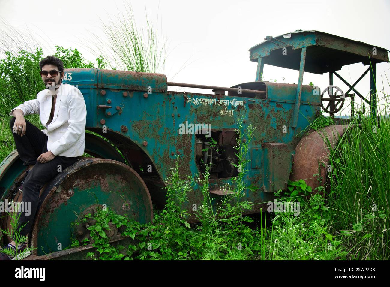 Modelli in posa in un campo aperto di fronte a un vecchio rullo. Il campo ha l'erba verde e sono vestiti in abiti bianchi e neri. Foto Stock