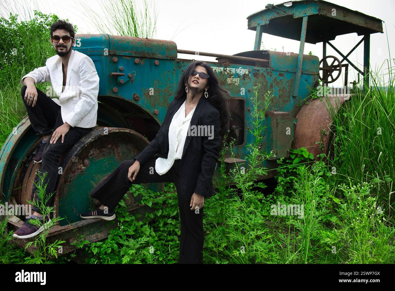 Modelli in posa in un campo aperto di fronte a un vecchio rullo. Il campo ha l'erba verde e sono vestiti in abiti bianchi e neri. Foto Stock