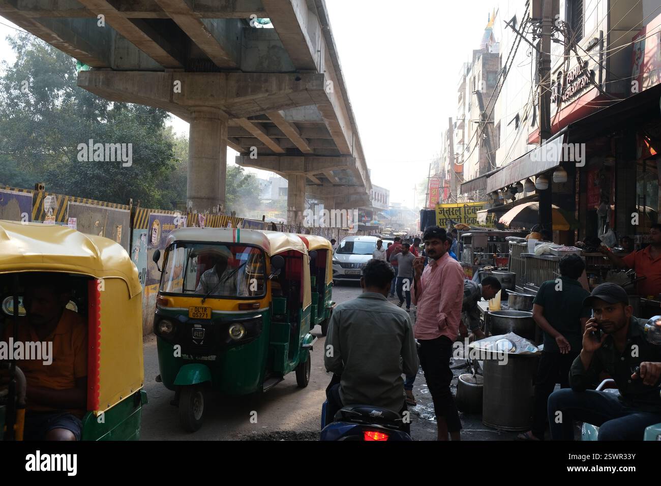 Autorickshaws passa accanto ai venditori di cibo di strada in una strada trafficata vicino alla stazione ferroviaria di Hazrat Nizamuddin nella capitale indiana Delhi Foto Stock