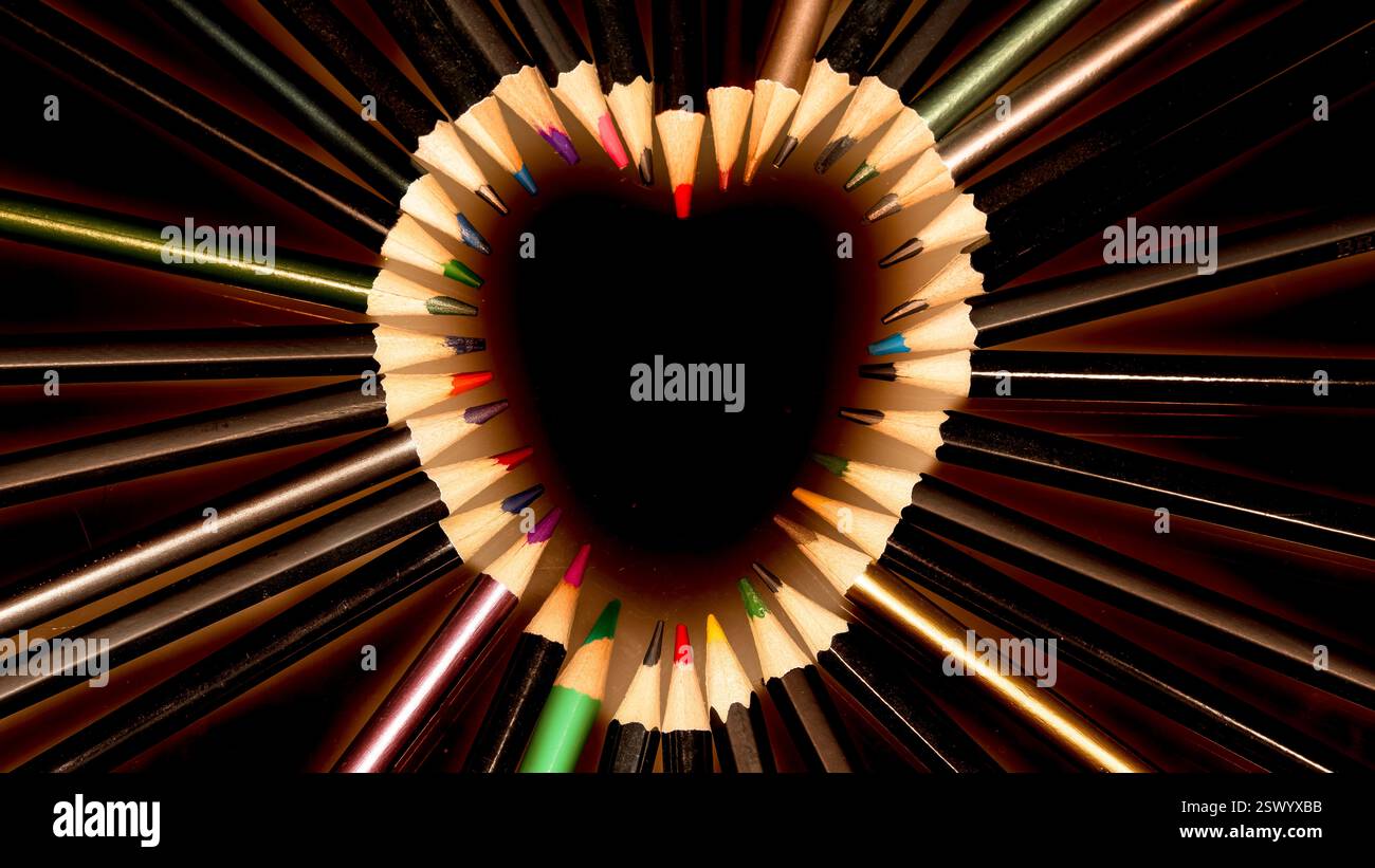 Punte a matita colorate a forma di cuore che formano un centro cavo con toni scuri e dettagli metallici in una composizione artistica creativa e simmetrica Foto Stock