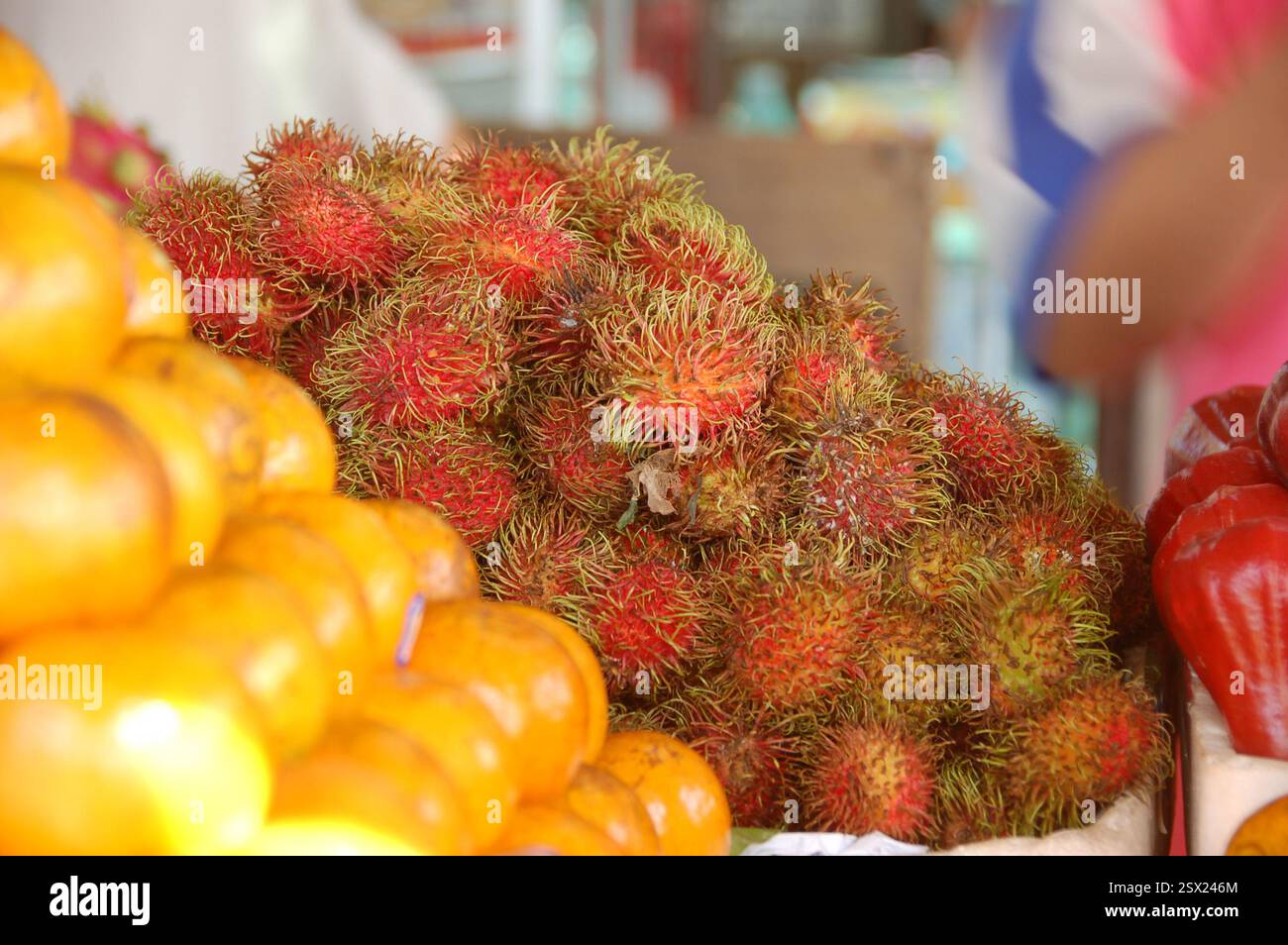 Una vivace bancarella di frutta in un mercato tailandese che mostra un mucchio di rambutani freschi insieme a una pila più piccola di arance, mostrando i prodotti esotici della Thailandia Foto Stock