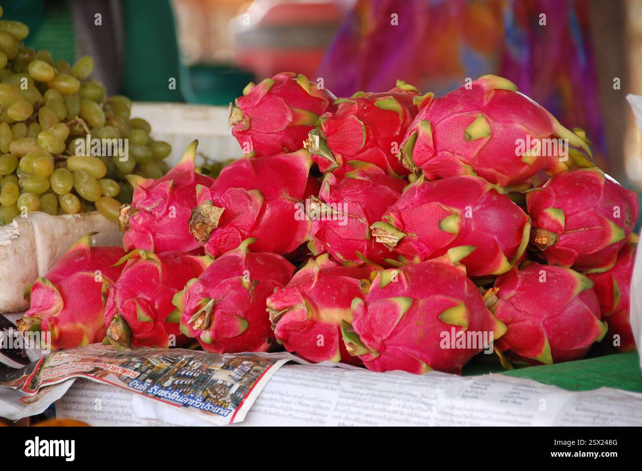 Un colorato banco di frutta in un mercato Tailandese caratterizzato da una grande pila di vibranti frutti del drago, che mostra i prodotti esotici e tropicali della Tailandia Foto Stock