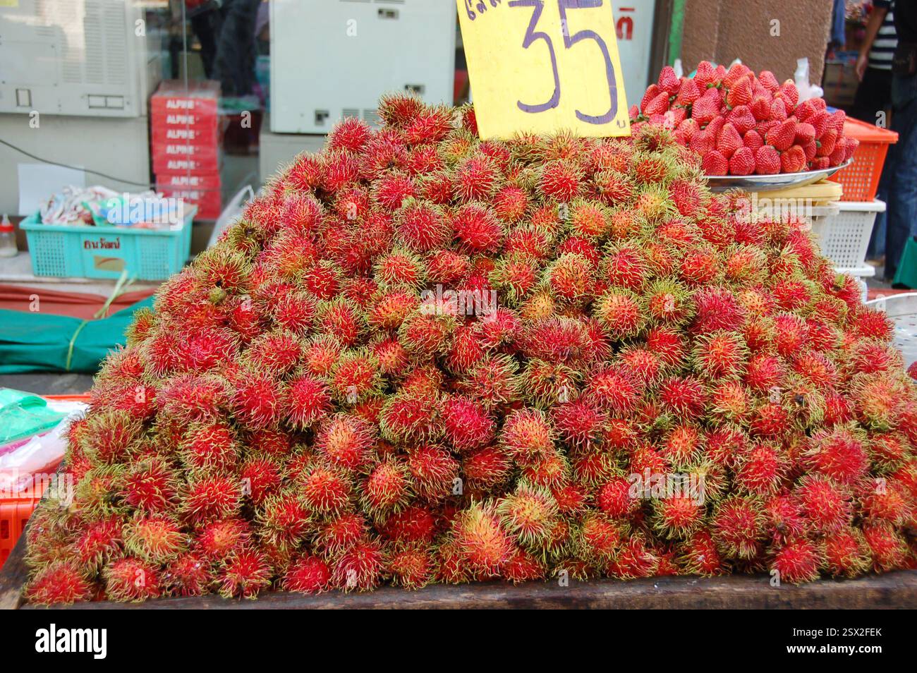 Una vivace bancarella di frutta in un mercato tailandese che mostra un mucchio di rambutan freschi con prezzi che mostrano i prodotti esotici della Thailandia al mercato di strada di Ayutthaya Foto Stock
