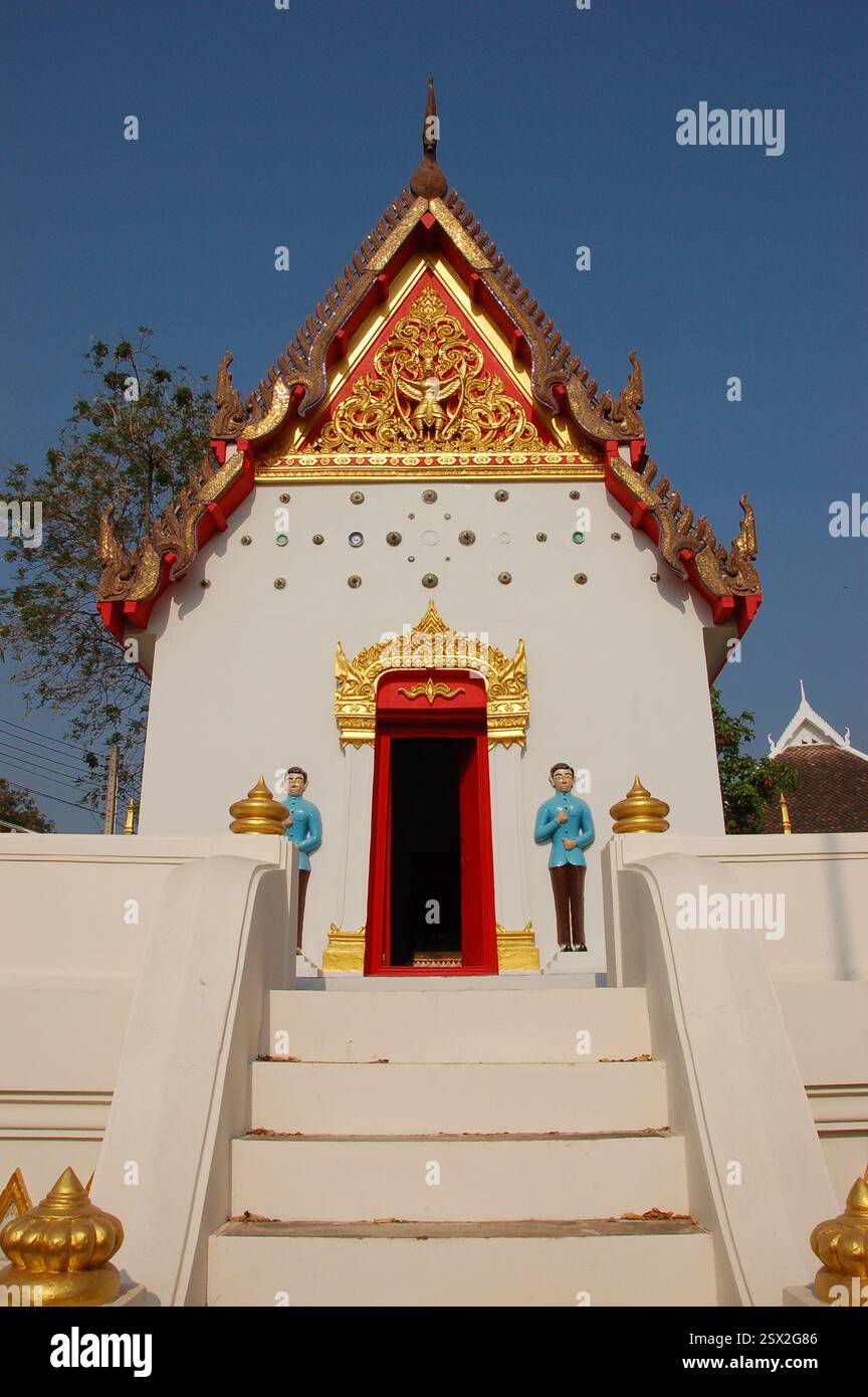 Il Santuario della colonna della città di Kanchanaburi, Thailandia, presenta un piccolo tempio bianco con i frontoni dorati, la tradizionale architettura Tailandese e la statua del guardiano Foto Stock
