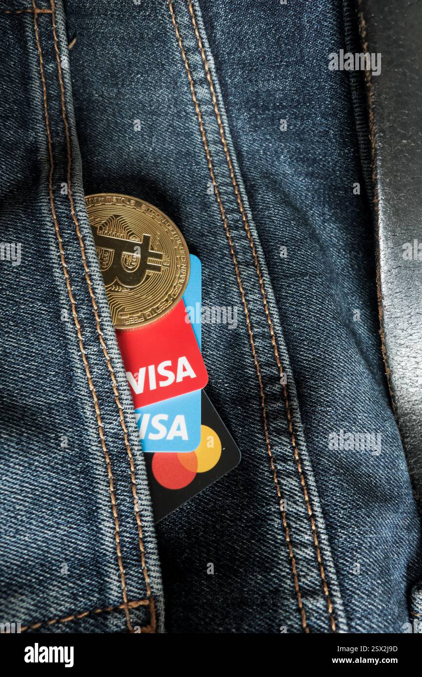 Venezia, Italia - 22 febbraio 2025: Carte di credito VISA e Mastercard accanto a una moneta fisica Bitcoin all'interno di una tasca di jeans blu a Venezia. Foto Stock