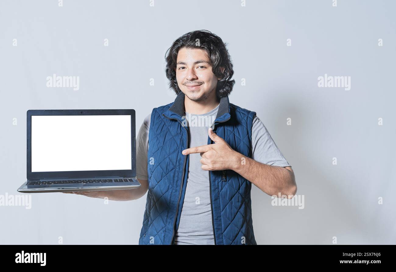 Un giovane sorridente che punta lo schermo del notebook isolato. Un ragazzo gentile che indica uno spazio vuoto sullo schermo del notebook Foto Stock